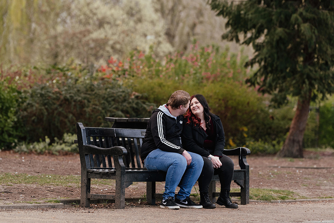 Couple sit looking at each other on bench Castle Park Engagement Session