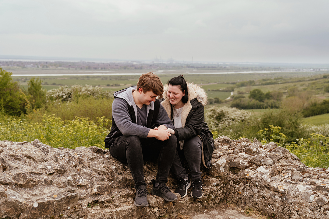 Couple sit on wall cuddled up overlooking the view Hadleigh Castle