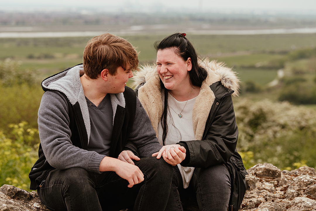 Couple sitting on wall close up laughing and looking at each other Hadleigh Castle