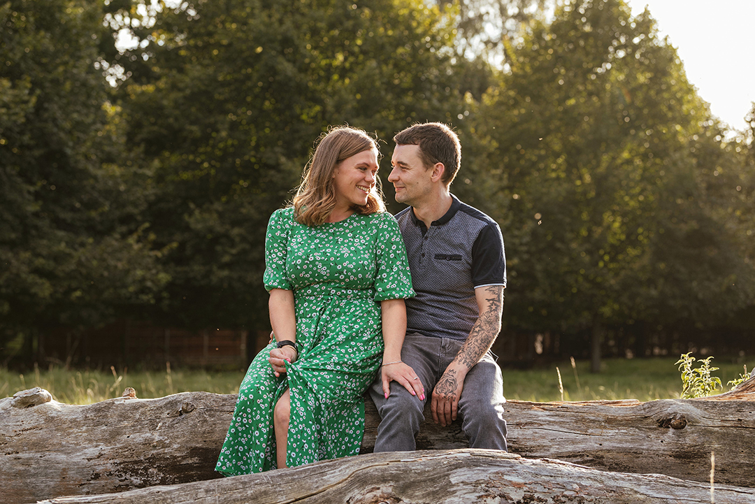 Couple sit facing each other on log Natural Engagement Session Pishiobury Park