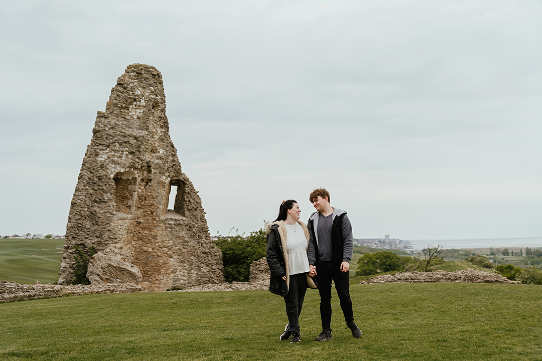Couple walk towards camera with castle remains in background Hadleigh Castle
