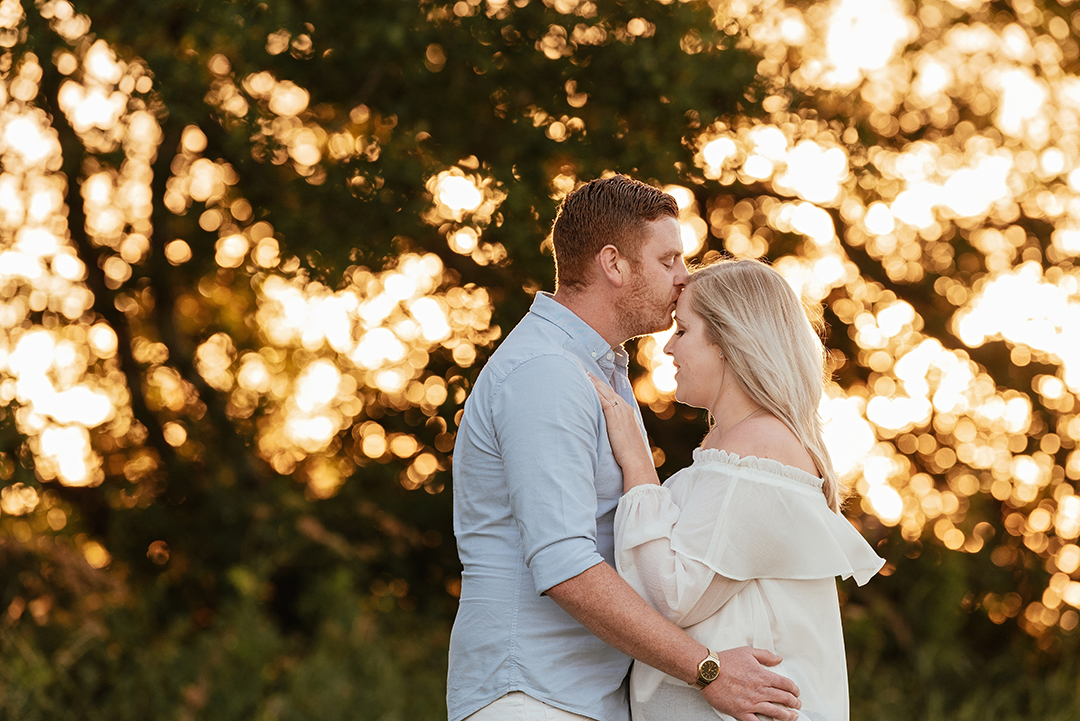 Beautiful sunset and couple embracing and he kisses her forehead Hylands Park Engagement Session