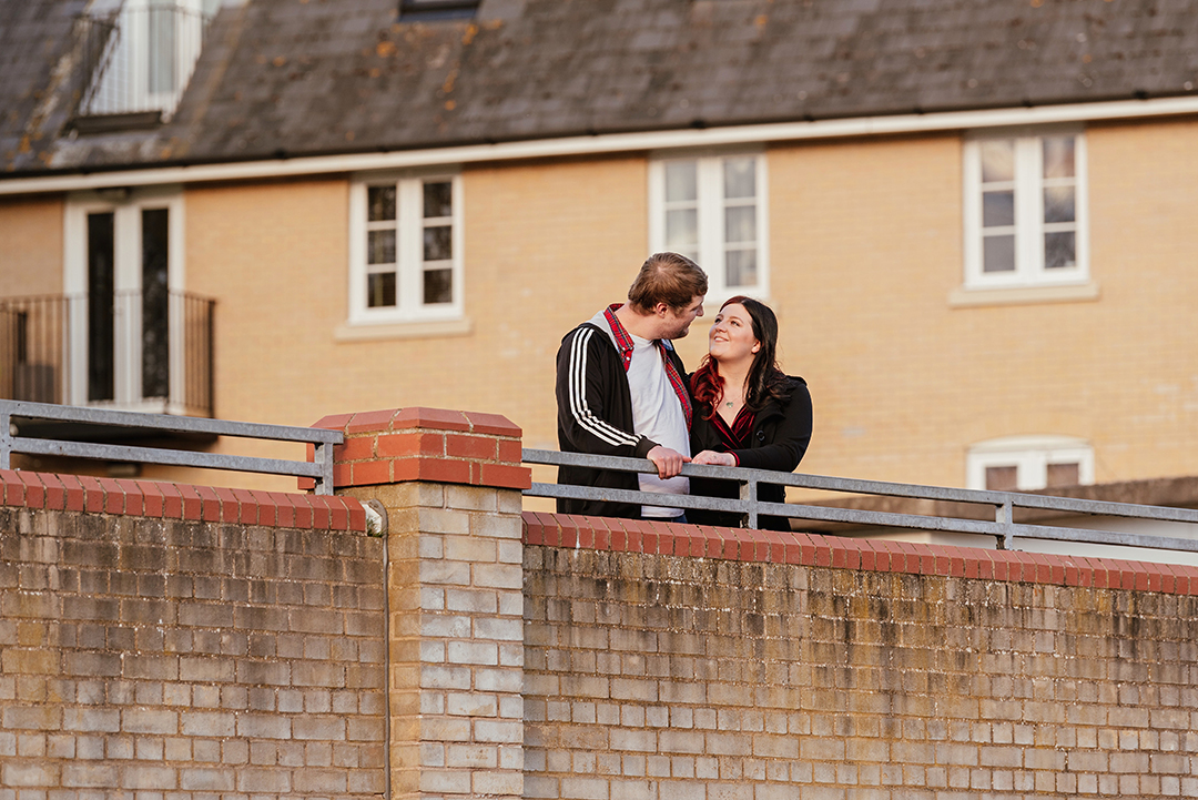 Couple look to each other on bridge in front of building Castle Park Engagement Photos