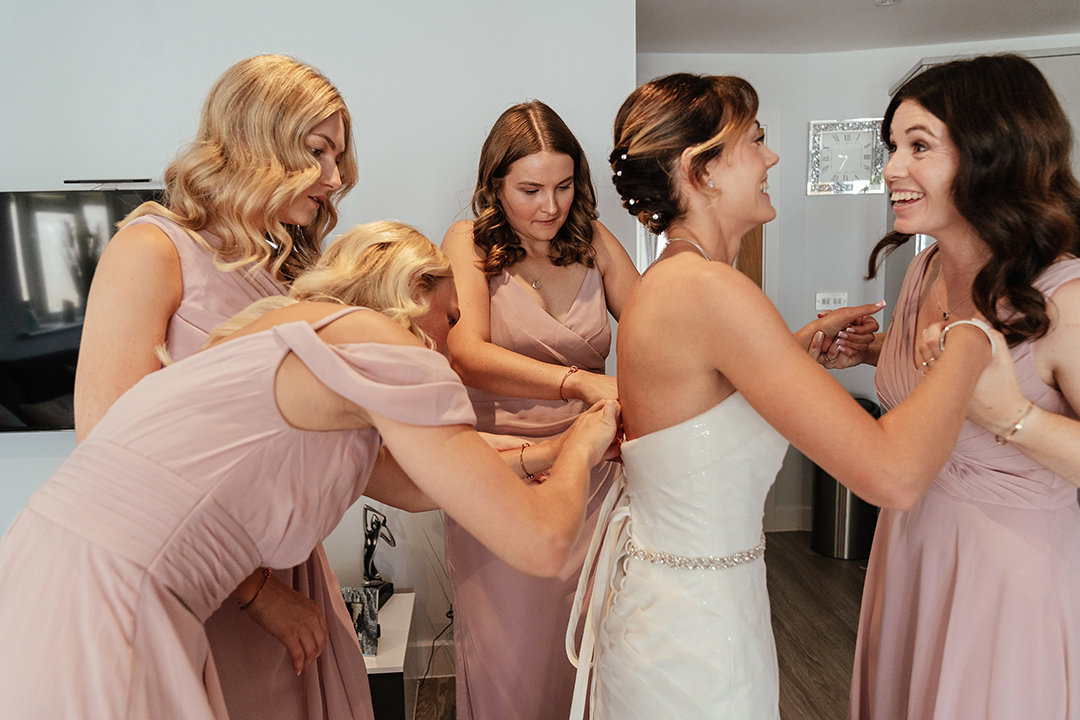 Bridesmaids Help Bride into Wedding Dress
