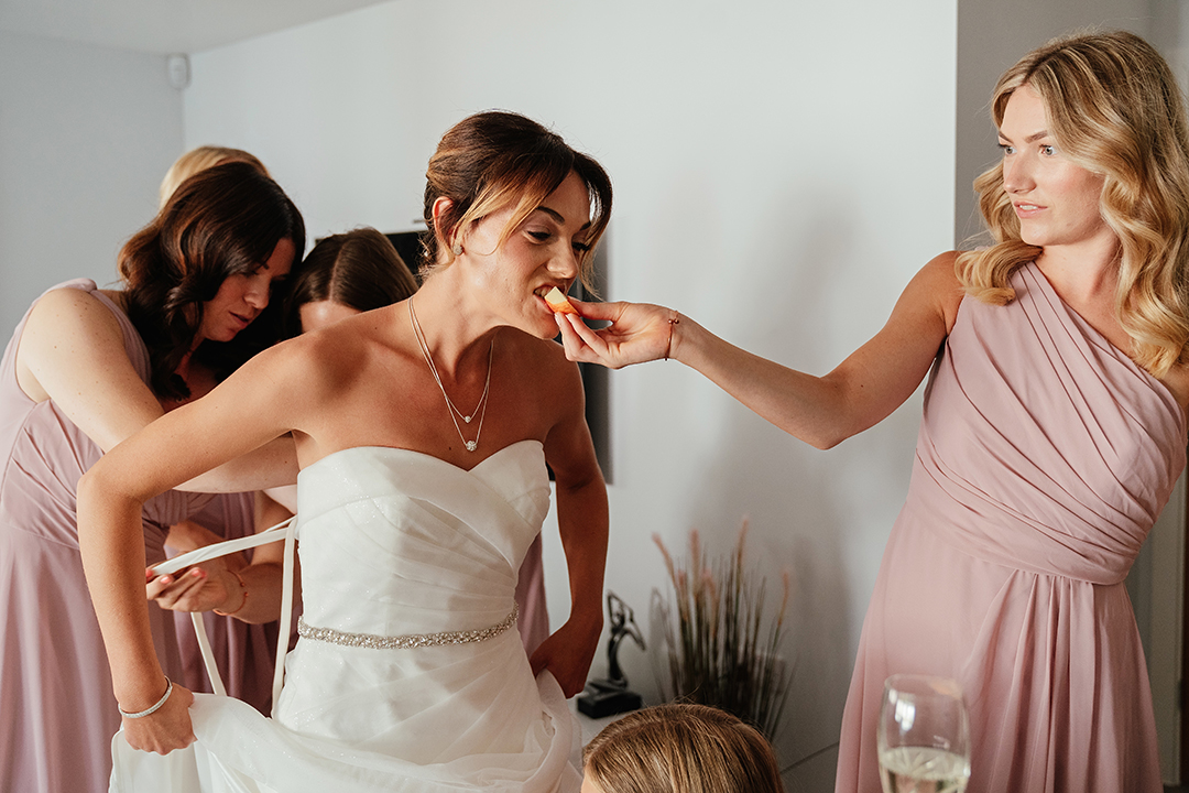 Bridesmaid Feeds Bride Some Fruit While Other Bridesmaids do Dress Up