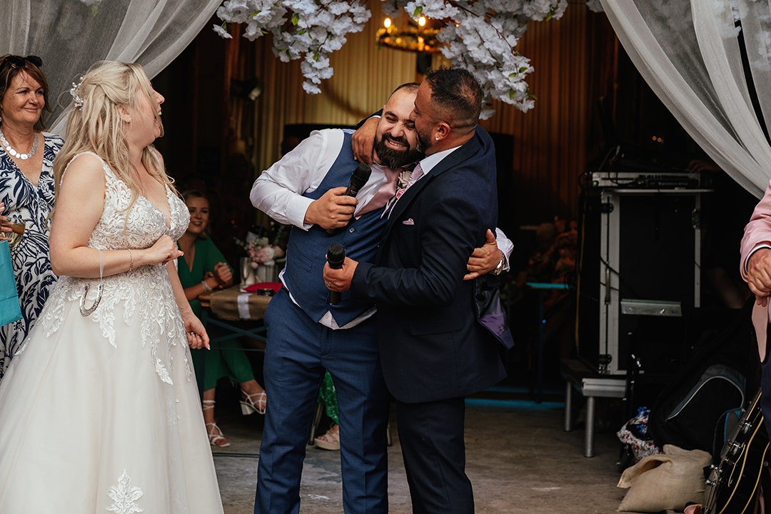 Groom kissing groomsmen during Mum gives funny towel to groom Speeches Stock Street Farm Barn Wedding