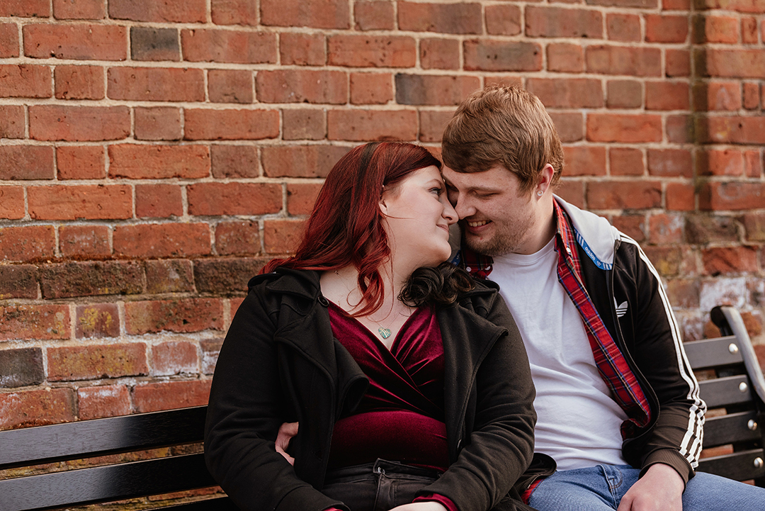 Couple sit on bench and intimately look to each other, heads together Castle Park Natural Engagement Shoot