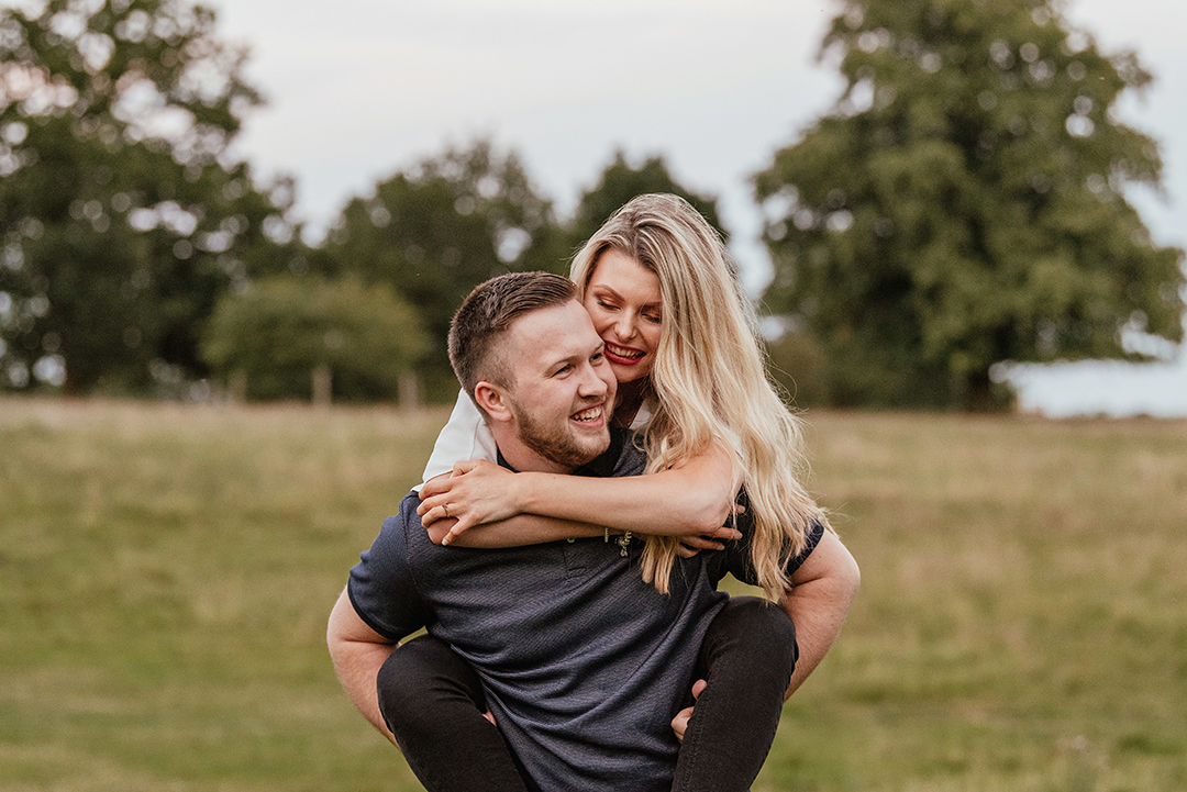 Couple give piggy back in Natural Pre wedding photo shoot at Pishiobury Park Essex