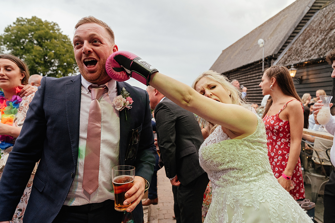 Bride pretends to punch guest with boxing glove, Stock Street Farm Barn Natural Relaxed Wedding Photography