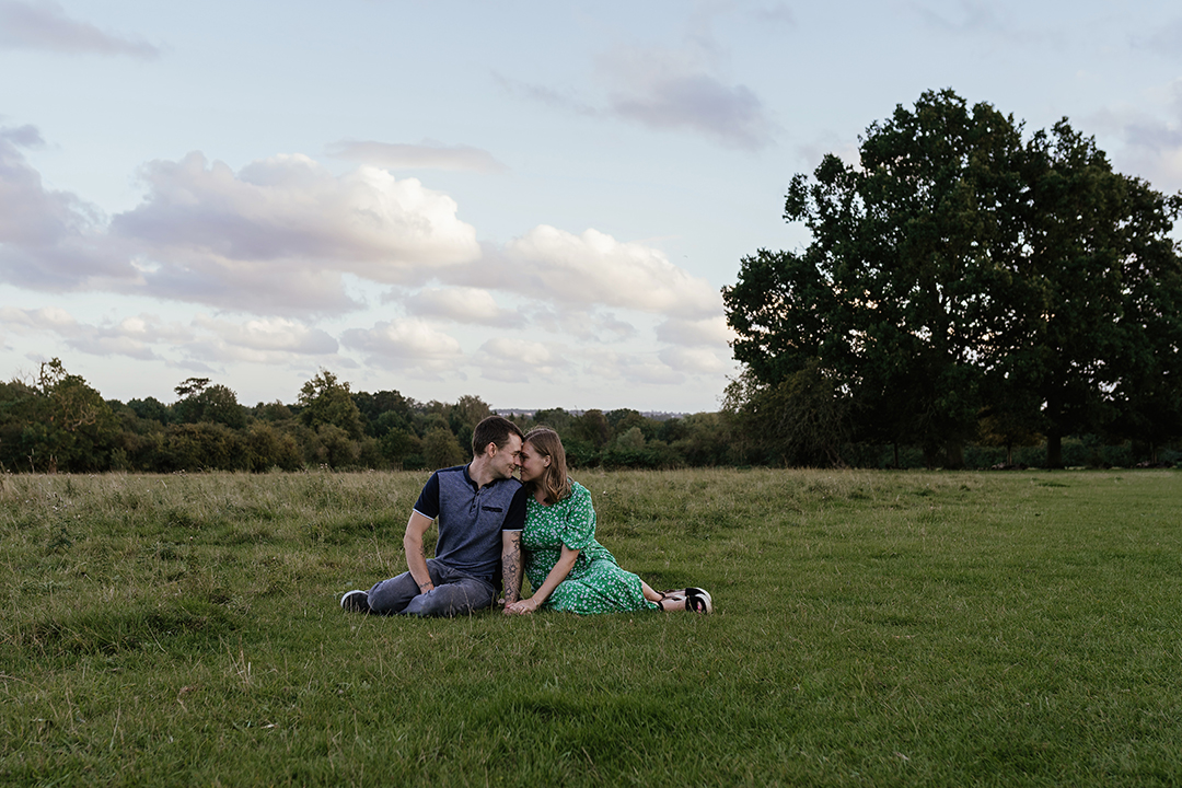 Couple sit in field together Pishiobury Park Engagement Shoot