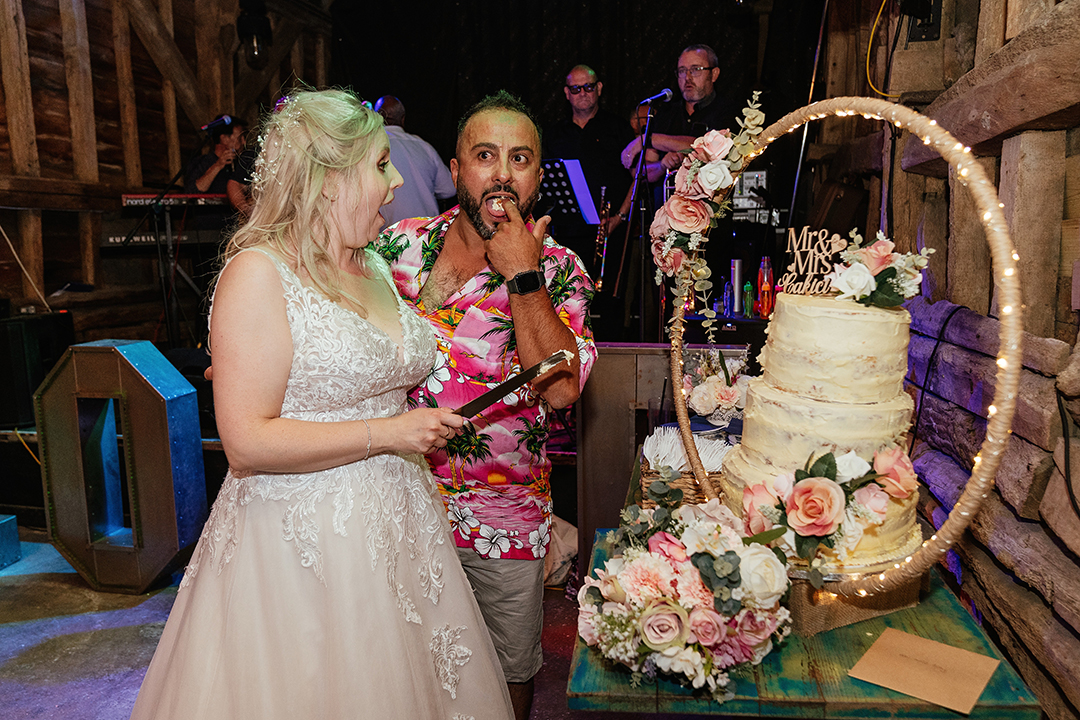 Bride and Groom in a Hawaiian Shirt try Wedding Cake at Stock Street Farm Barn Wedding