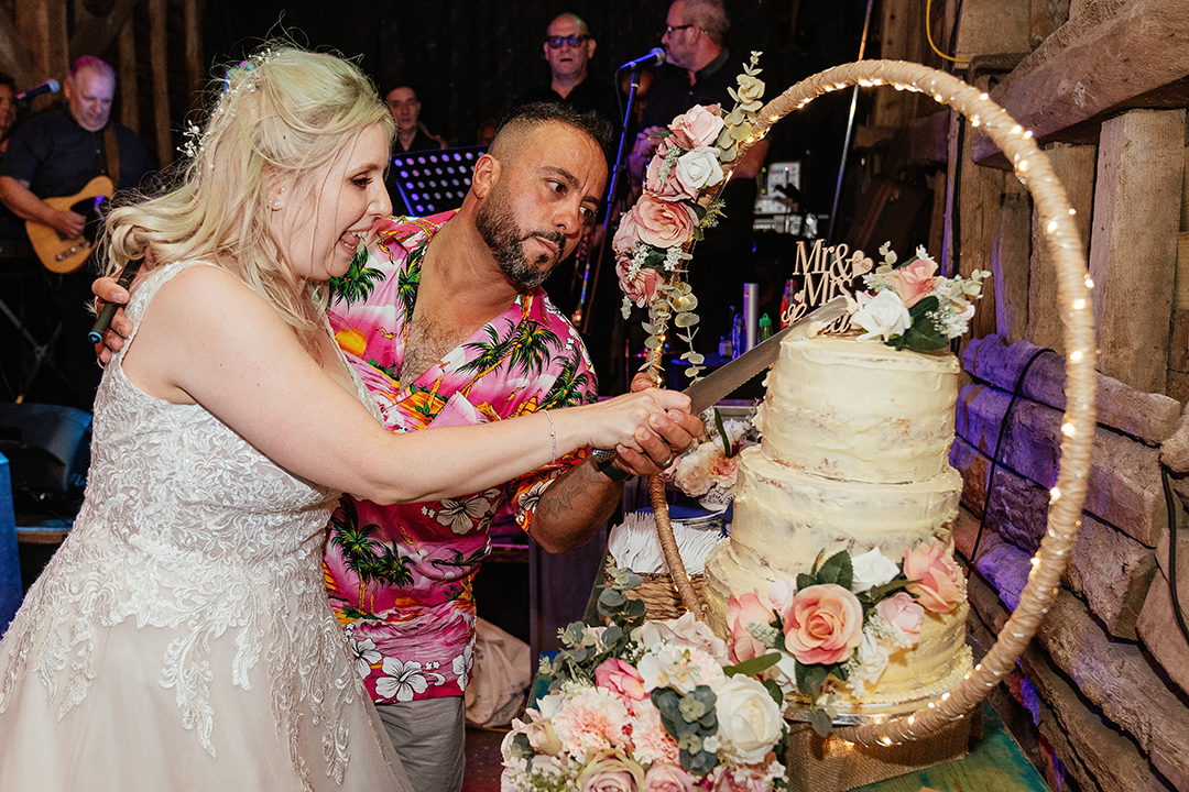 Bride and Groom in a Hawaiian Shirt Cutting Wedding Cake at Stock Street Farm Barn Wedding