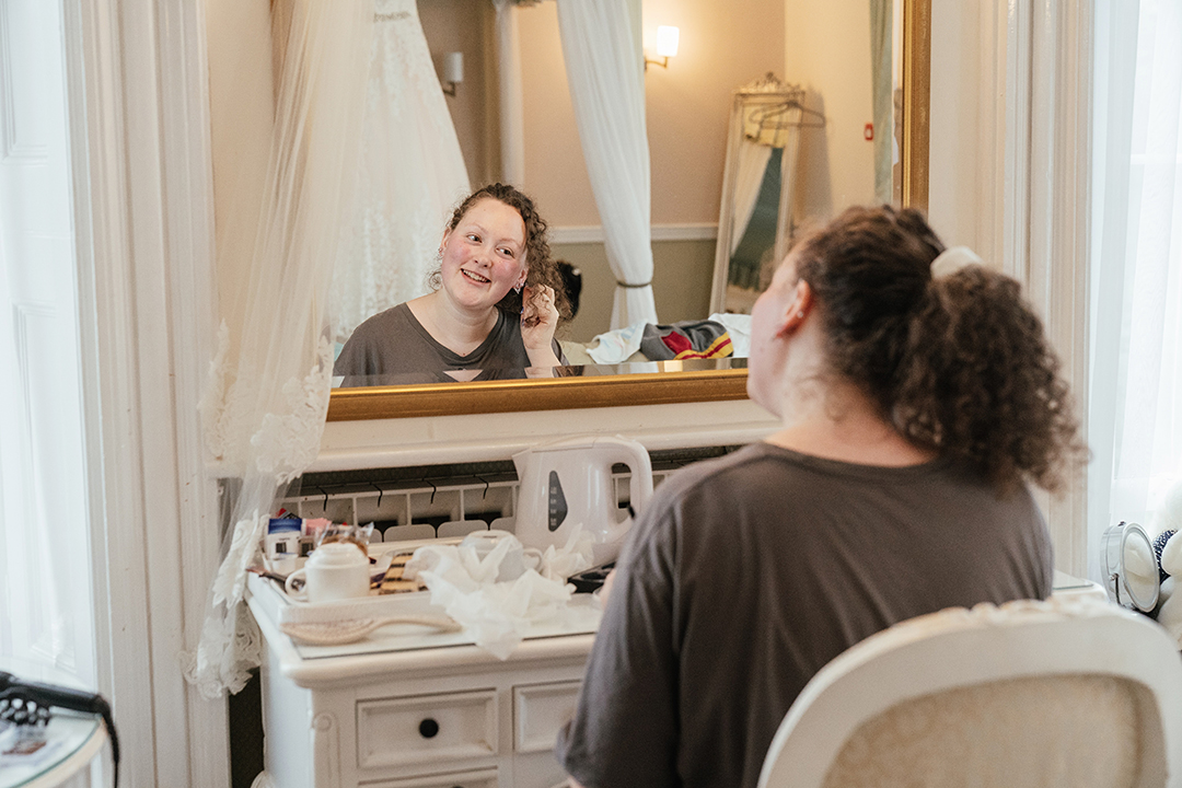 Getting Ready Bride Sits and Looks into Mirror at Manor of Groves Wedding