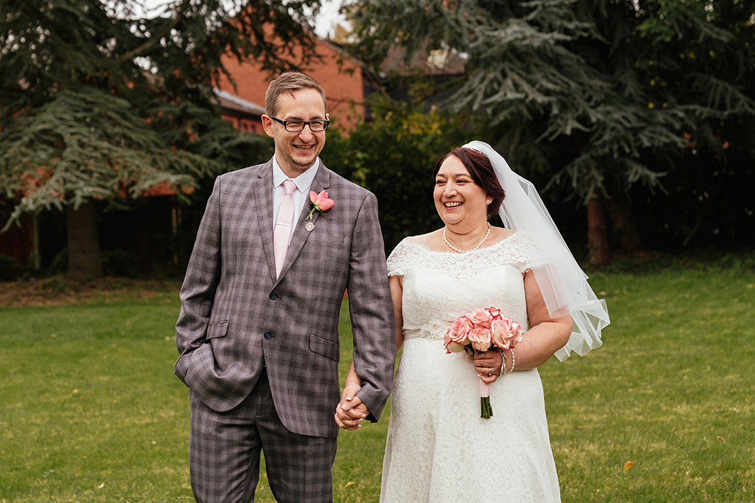 Half length of Couple walk towards camera with evergreen trees in background at Moot House Wedding Harlow