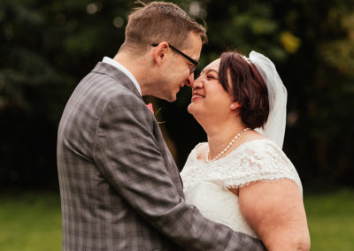 Couple give each other eskimo kisses with evergreen trees in background at Moot House Wedding Harlow