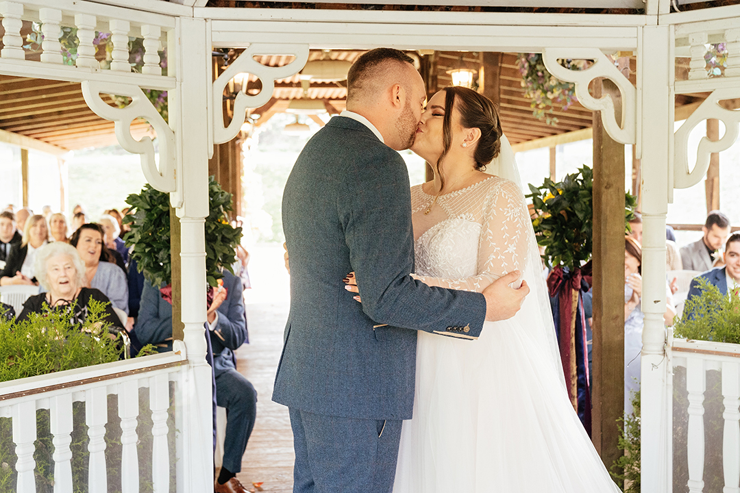 Bride and groom hold each other and share first kiss under gazebo at Minstrel Court Wedding Ceremony