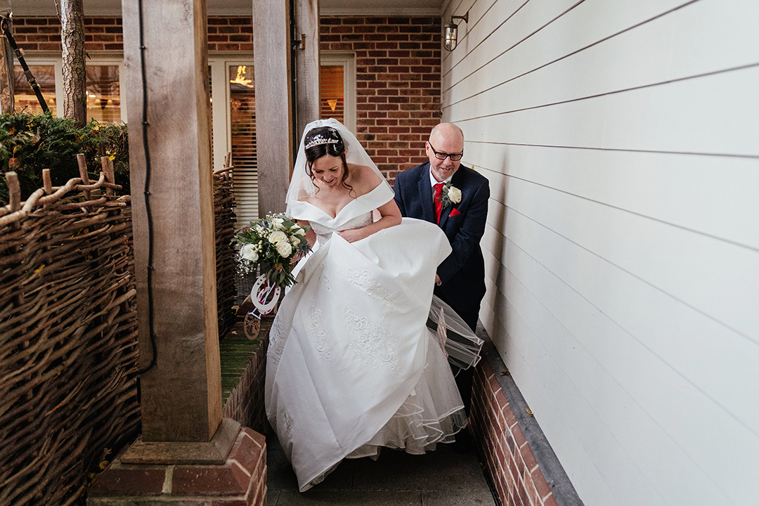 Groom helps bride with dress as they walk towards the camera Natural Wedding Photography at the Lion House