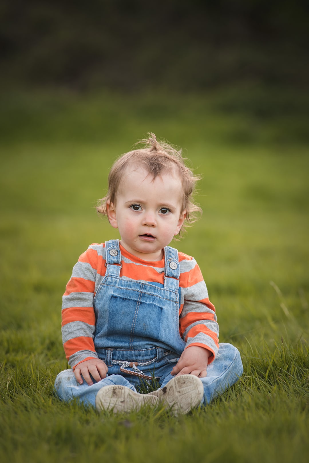 Cute baby girl sitting in grass looking at camera