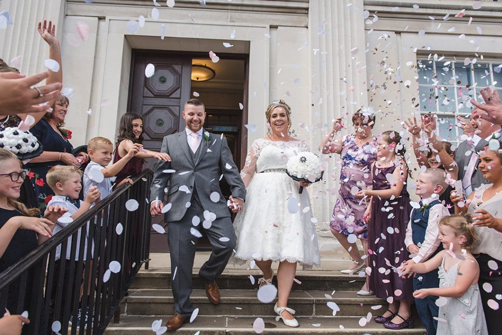 Essex wedding photographer captures Bride and groom walking down the steps while guest throw confetti