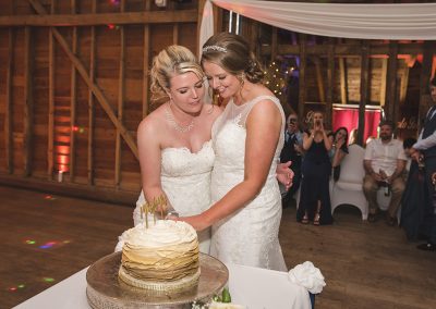 Two brides cut their Mrs and Mrs wedding cake with rainbow colours inside