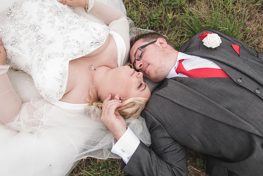 Bride and Groom laying in the grass heads tilted lovingly towards each other