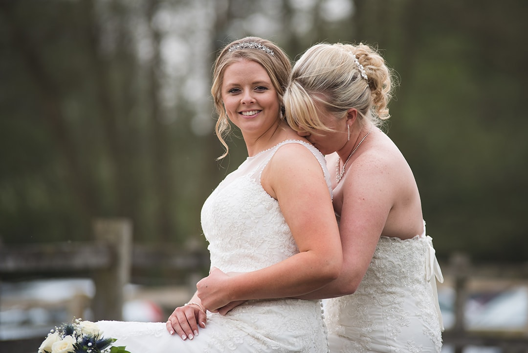 Gorgeous natural portrait of two brides embracing while sat on bride at Tewin Bury Farm Hotel