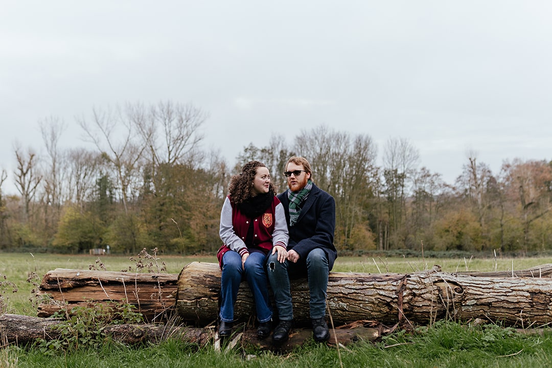Sitting on a log together in country park engagement photo shoot