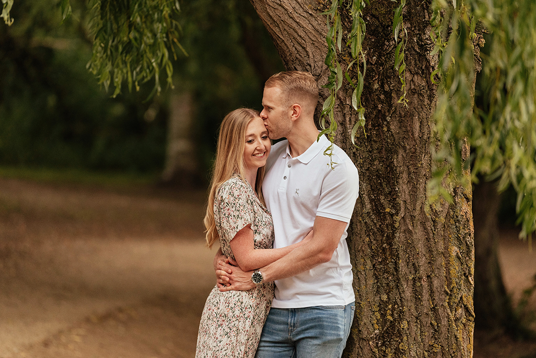 Couple lean against tree laughing and hugging at Stanborough Lake Couples Photos