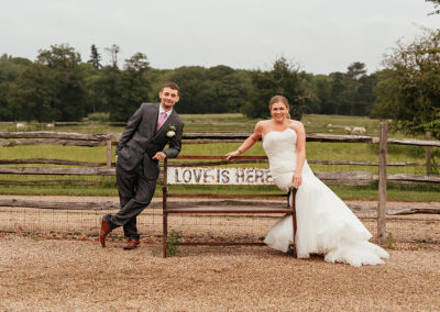 Couple sit either side of bench that reads Love is Here at Gaynes Park