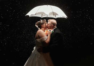 Couple kiss under umbrella in rainy wedding photos