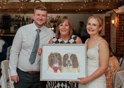 Couple stand with guest who painted them a photo of their dogs