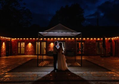 Night time shoot outside fairylit venue with couple backlit