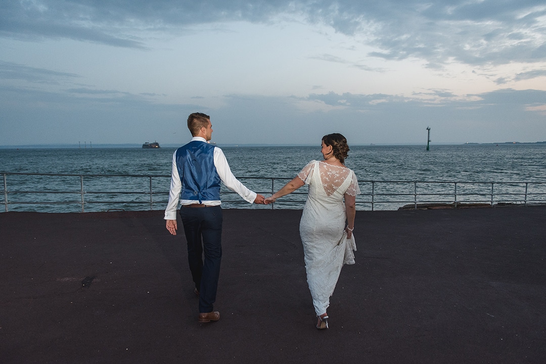 Cute natural image of bride and groom walking away from camera towards the sea